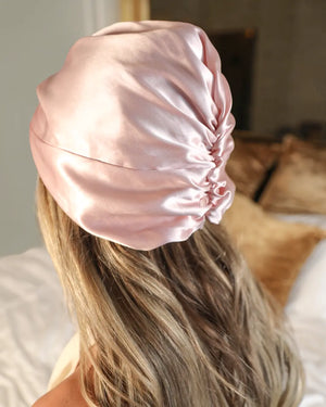 Back view of a woman wearing a pink Lenoites Mulberry Silk Sleeping Cap, showing smooth, shiny hair protected by 100% soft silk material.