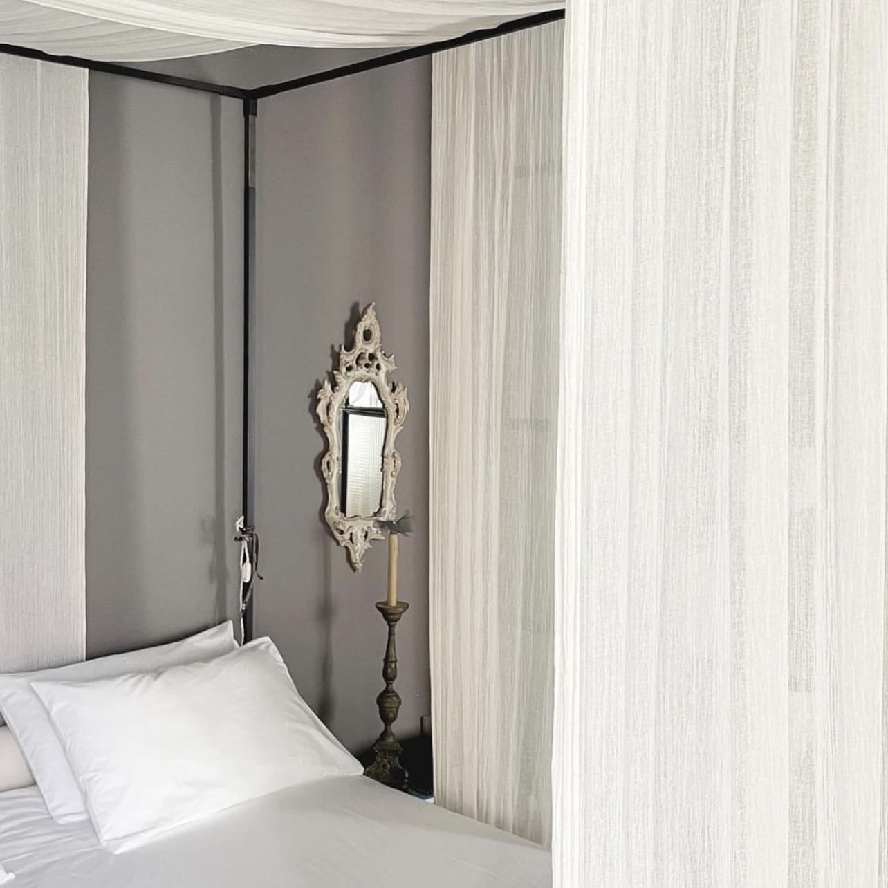 sovrum med vita påslakan och vitt sidenörngott med spegel på väggen och sänghimmel